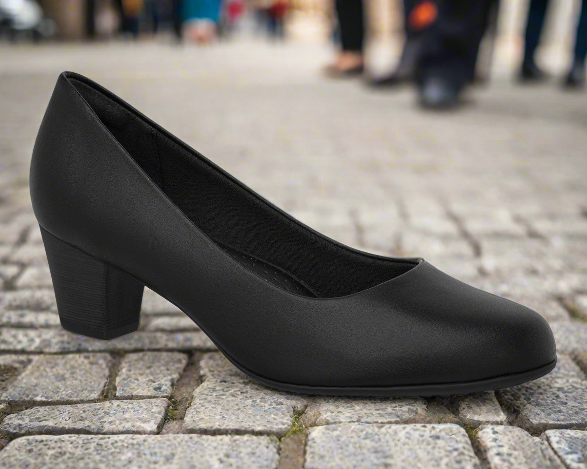A single black Piccadilly Ref: 439A Flight Attendant Terminal & Cabin Shoe, made for airline crew comfort, sits on a cobblestone street with blurred people in the background.